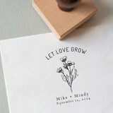 A custom wedding stamp with a floral design and the text 'LET LOVE GROW' along with personalized names and a date stamped on a piece of paper.