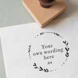 A circular rubber stamp with leaf patterns, placed on a piece of white paper with the words 'YOUR WORDING HERE'