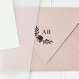 A custom rubber stamp with initials 'AR' and a floral design, pressed onto a pink envelope, creating a black monogram stamp impression.