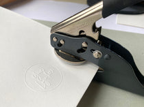 Handheld embosser seal creating a custom logo impression on white card