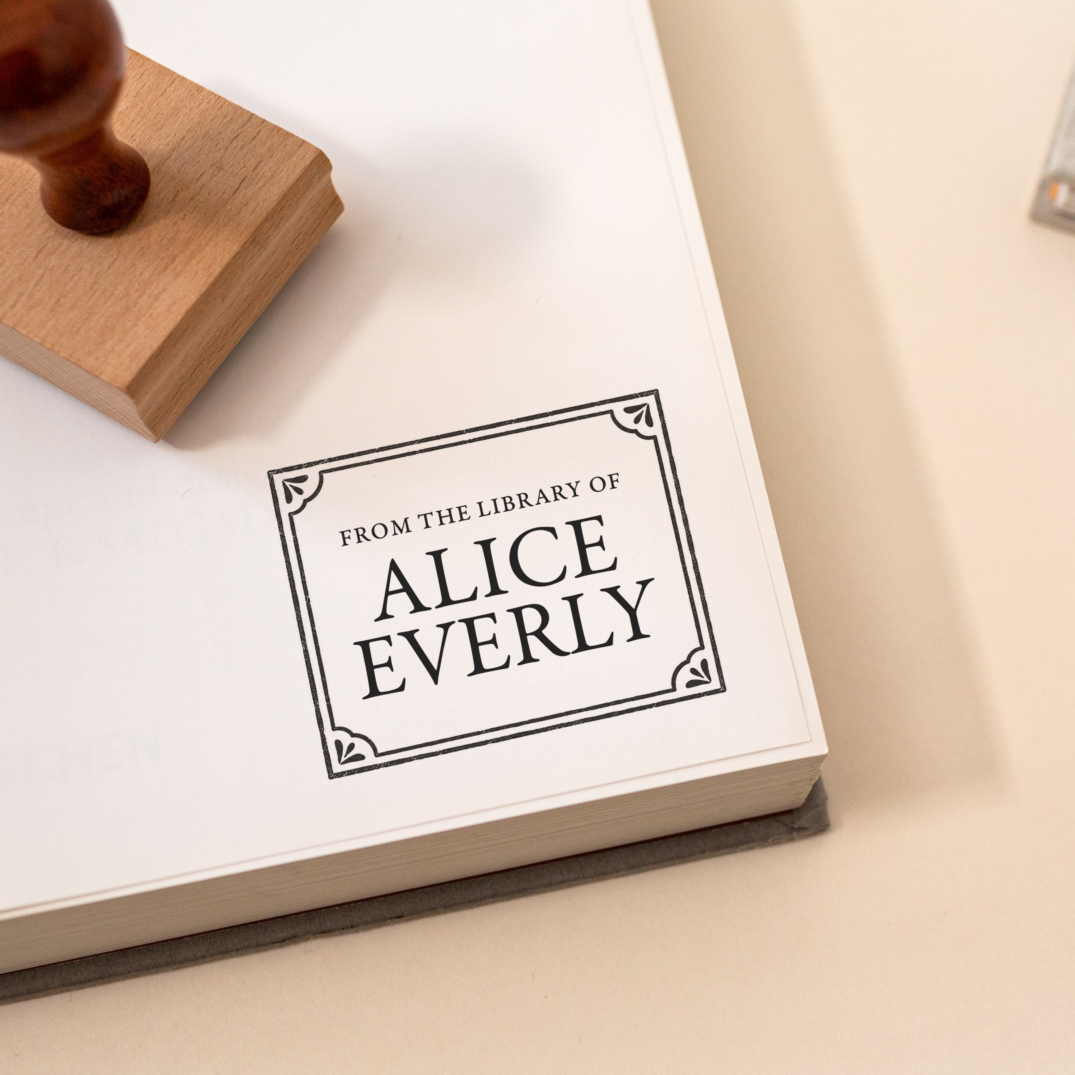 Personalised vintage library stamp on a book page, featuring classic lettering and delicate floral corner details.