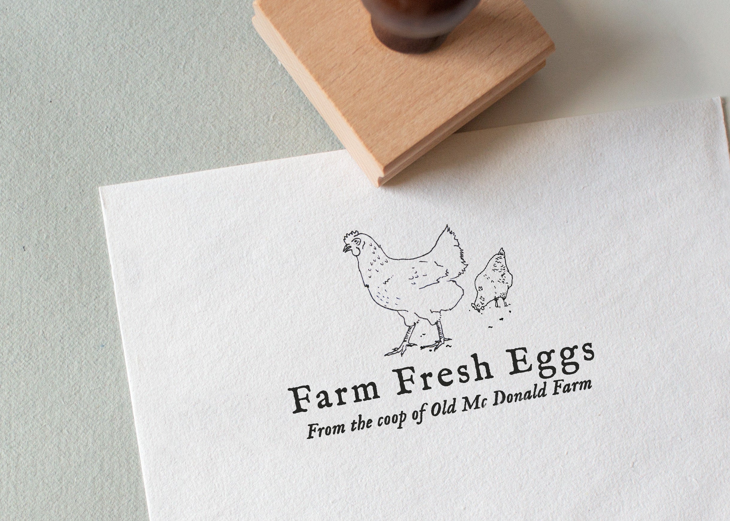 textured paper with the wording 'Farm Fresh Eggs' and chicken illustration stamped on white textured paper