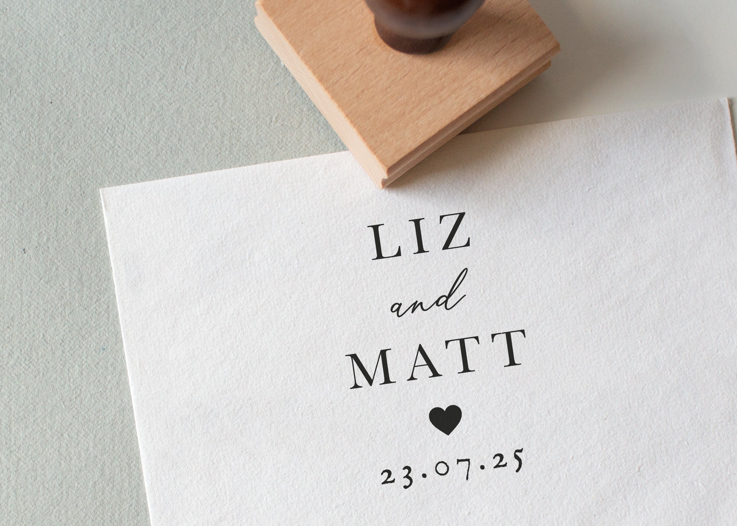 Personalised wooden wedding stamp with couple’s names, date and heart, stamped on white textured paper