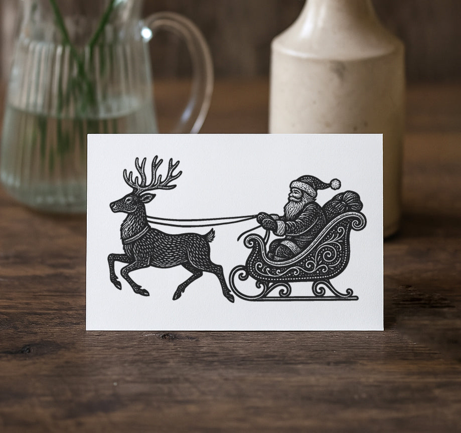Greeting card with black and white illustration of Santa Claus in a sleigh pulled by reindeer on a wooden surface.