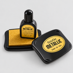 StazOn Metallic Gold ink bottle and matching black stamp pad with a black ink pad, shown on a light gray background.
