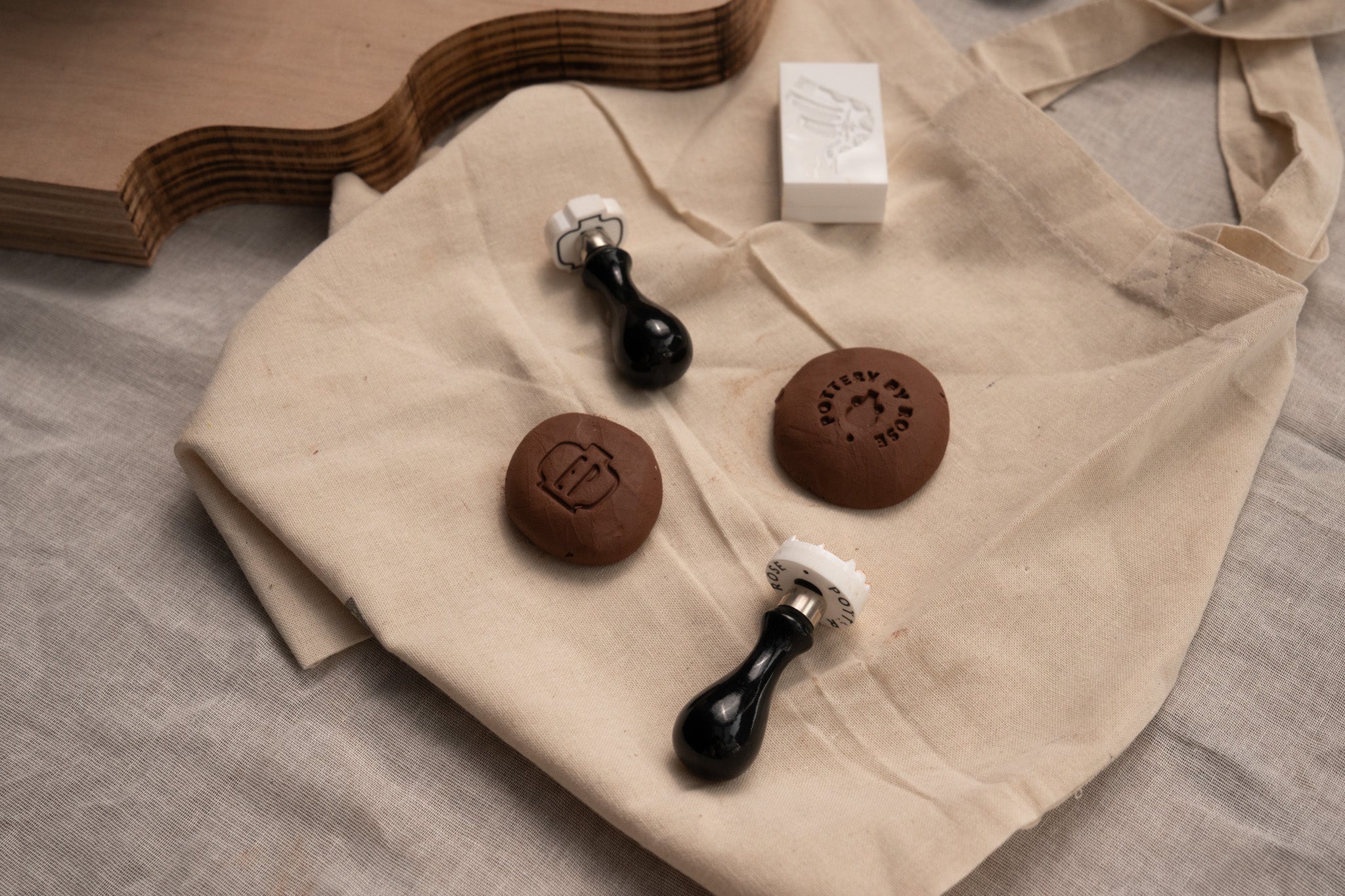 Two custom pottery stamps or makers marks next to two pieces of clay with clay logo impressions 