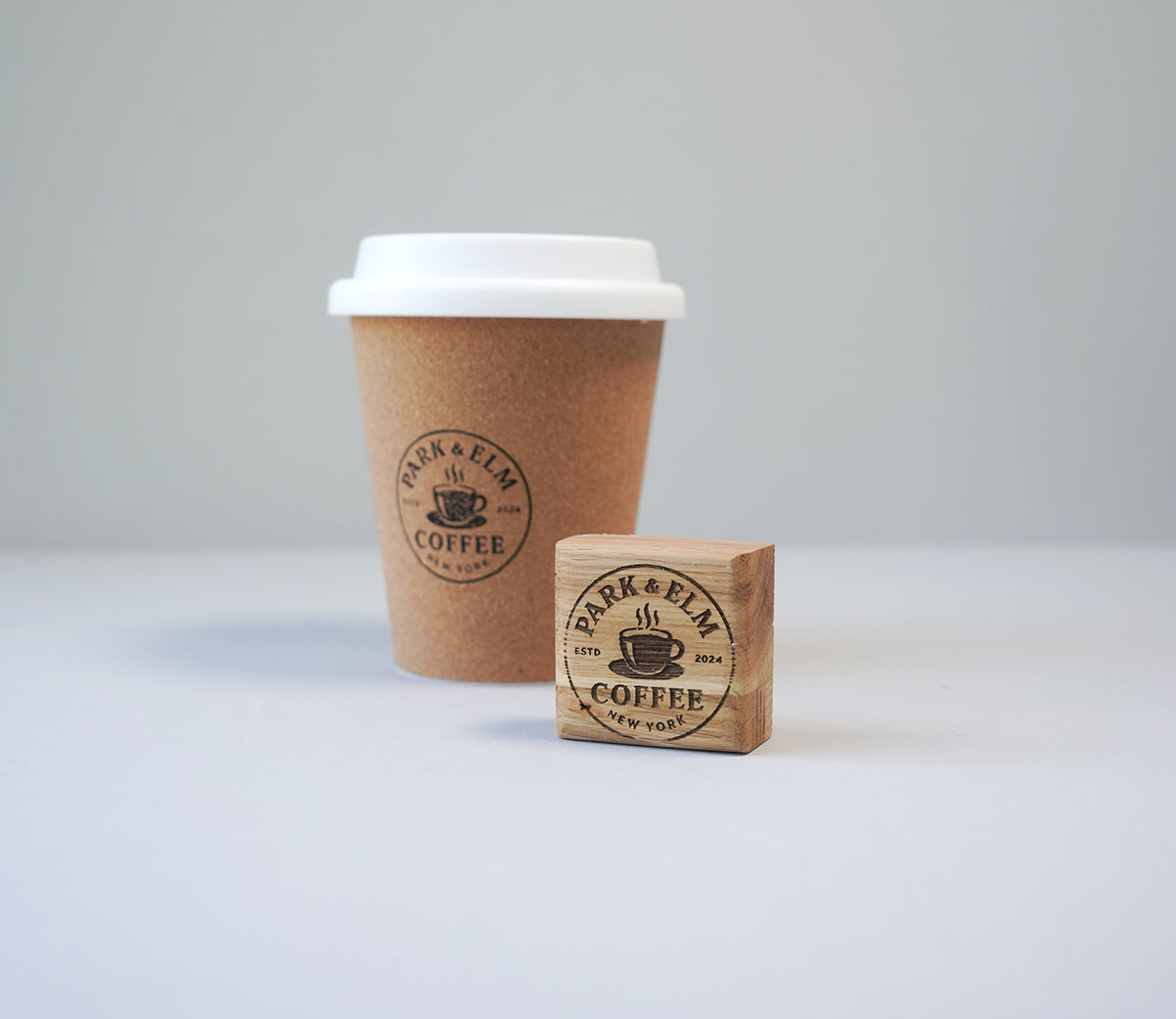 A custom coffee cup rubber stamp with an ink pad, showing a imprint of a coffee shop logo on a disposable coffee cup with a lid.