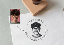 custom rubber portrait stamp with a stamped portrait illustration and 'the wording Approved by Jonathan Newman'  on a paper surface.