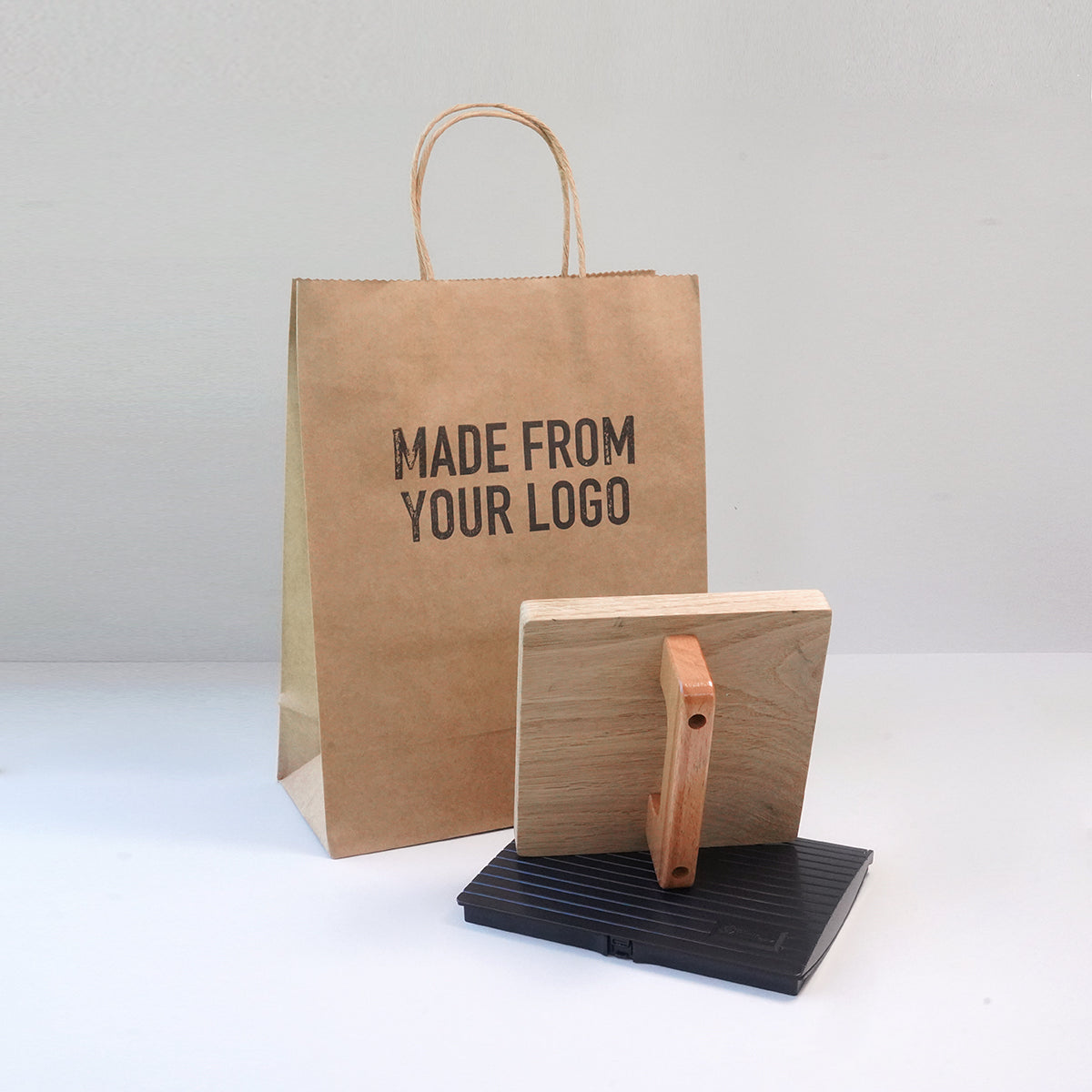 Kraft paper bag with 'MADE FROM YOUR LOGO' text and a large custom rubber stamp on a white background
