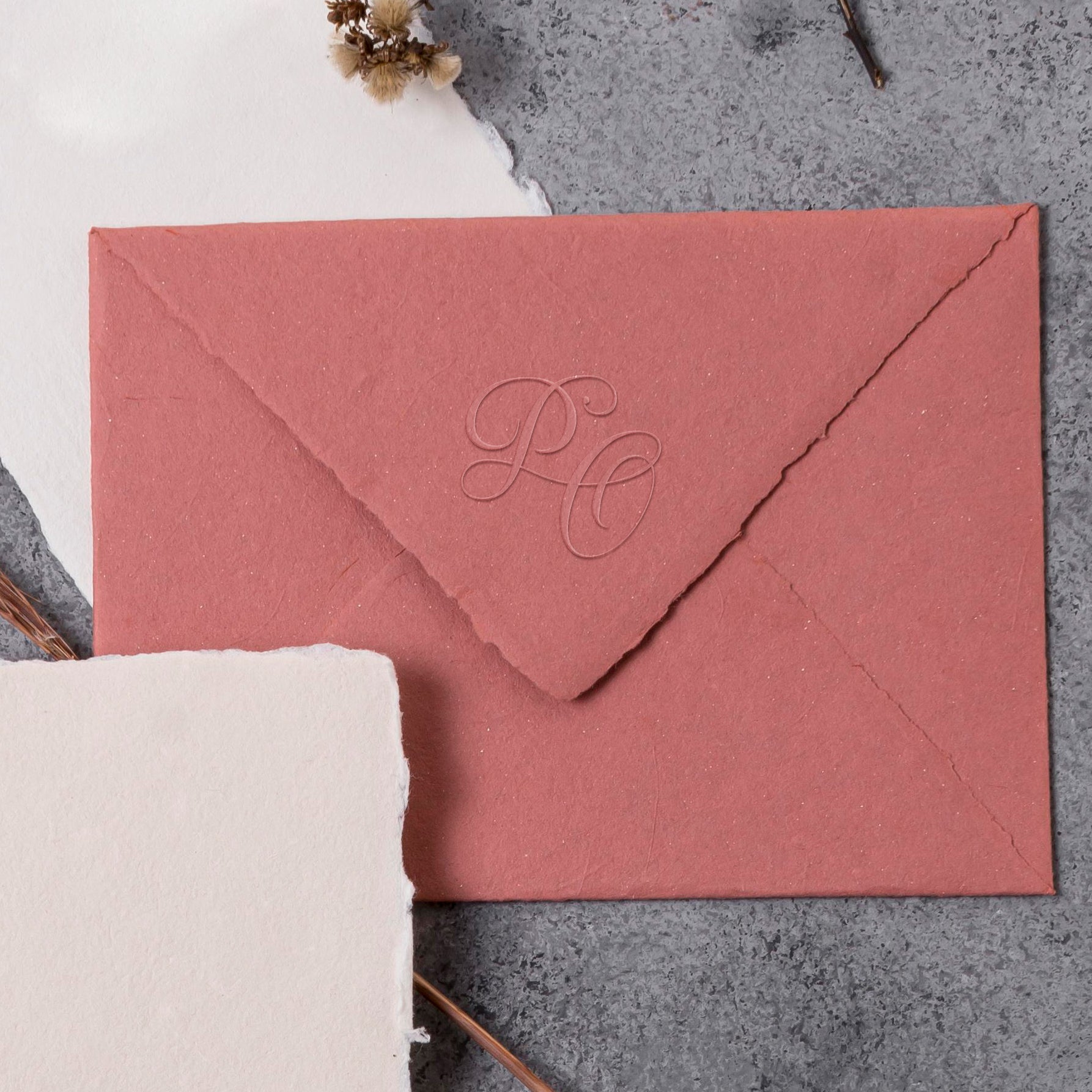 Close-up of wedding stationery with modern embossed initials in a calligraphic style.