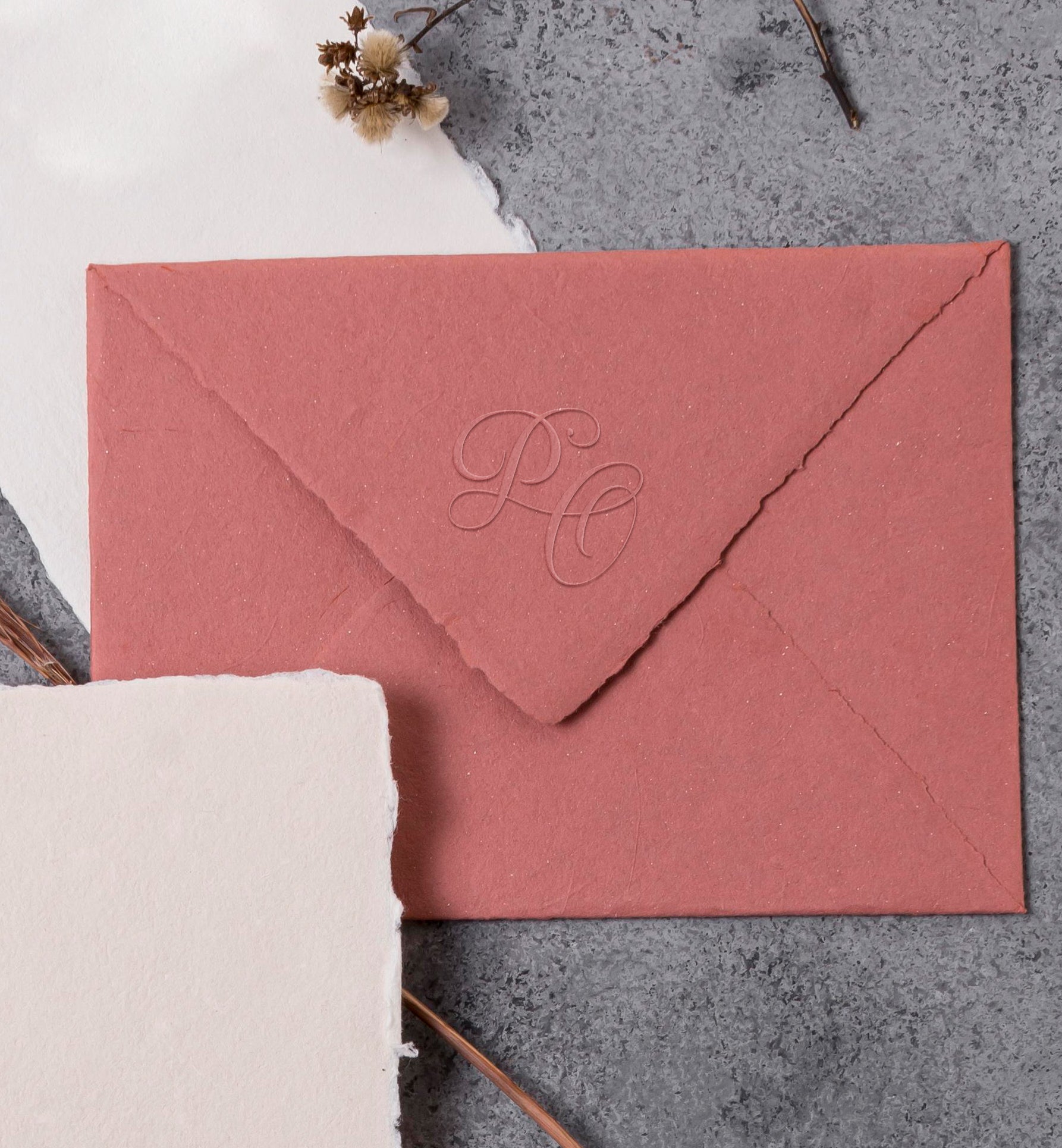 Close-up of wedding stationery with modern embossed initials in a calligraphic style.