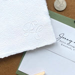 Close-up of wedding stationery with modern embossed initials in a calligraphic style.