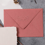 Embossed impression of a beautiful poppy flower and a couples initials onto a red wedding envelope