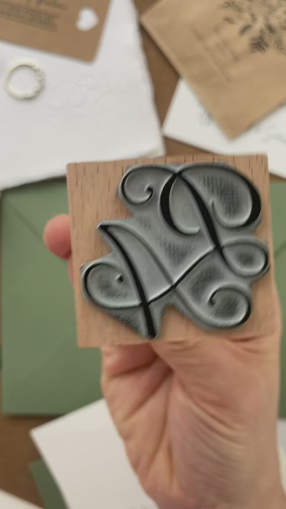 Wedding initials rubber stamp featuring the letters P & A in an elegant calligraphic script, leaving a crisp stamped impression on a green envelope.