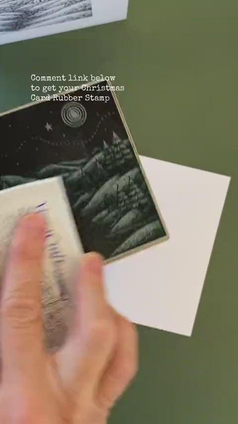 A large rubber stamp featuring a winter scene of the countryside stamping on a white christmas card