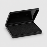 A black rectangular ink pad case shown open, revealing a textured black ink pad inside, set against a light gray background.
