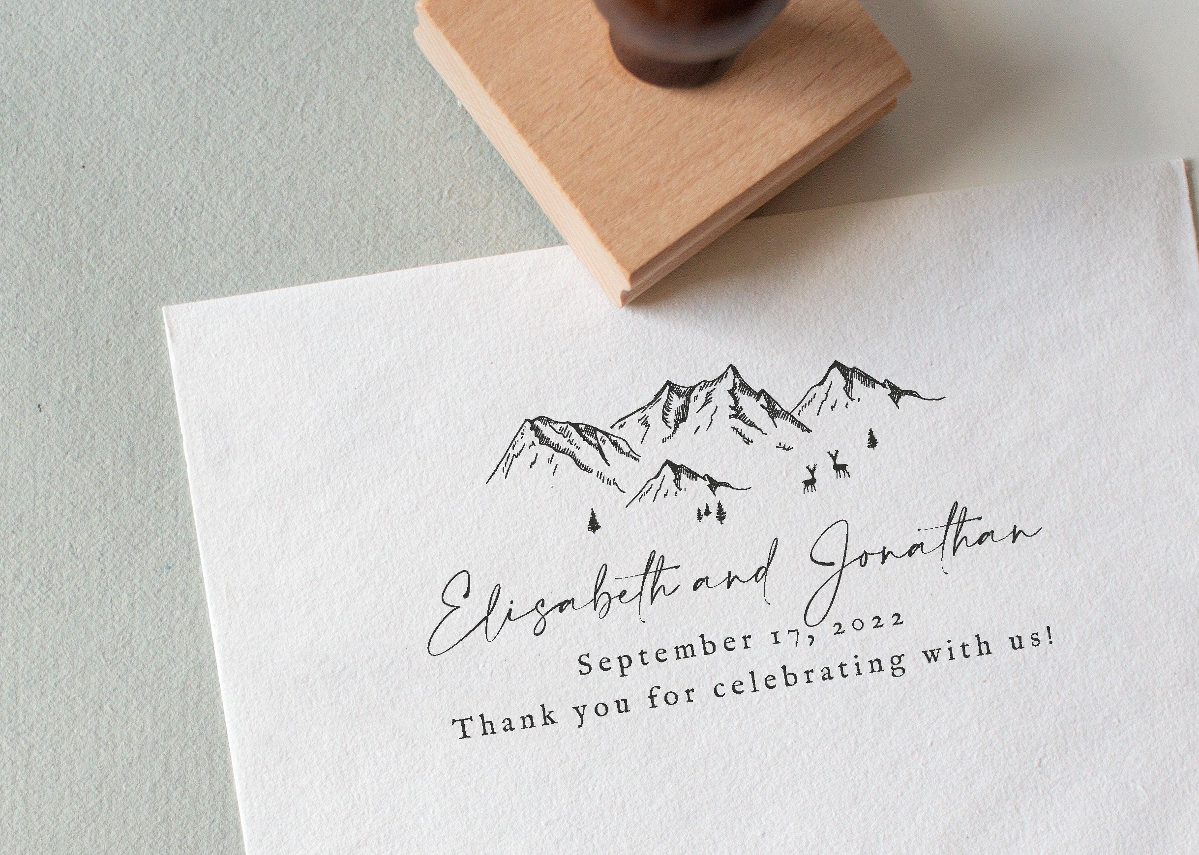 A custom wedding stamp with a mountain design being used on a piece of paper to create an impression that includes personalized text.