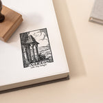 A custom library stamp with a vintage countryside book stamp design, stamped on an open book with a wooden stamp on the side.