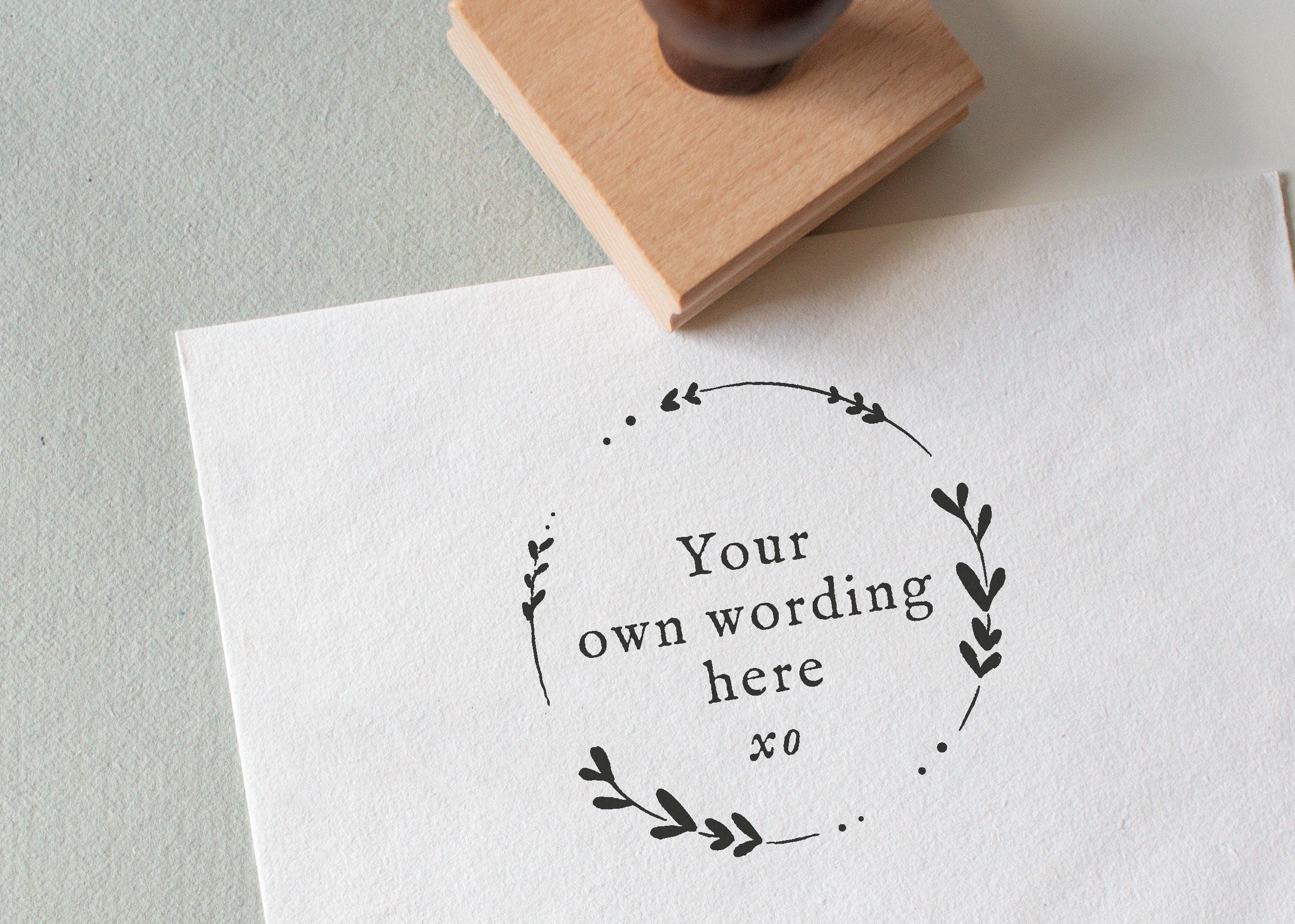 A circular rubber stamp with leaf patterns, placed on a piece of white paper with the words 'YOUR WORDING HERE' 