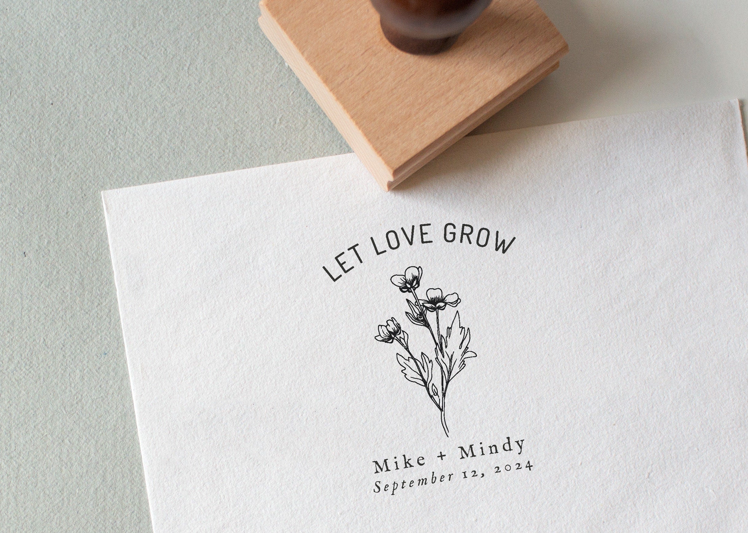 A custom wedding stamp with a floral design and the text 'LET LOVE GROW' along with personalized names and a date stamped on a piece of paper.