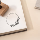 A custom library stamp with a design of a flower library motif, placed on an open book with a wooden handle on the side.