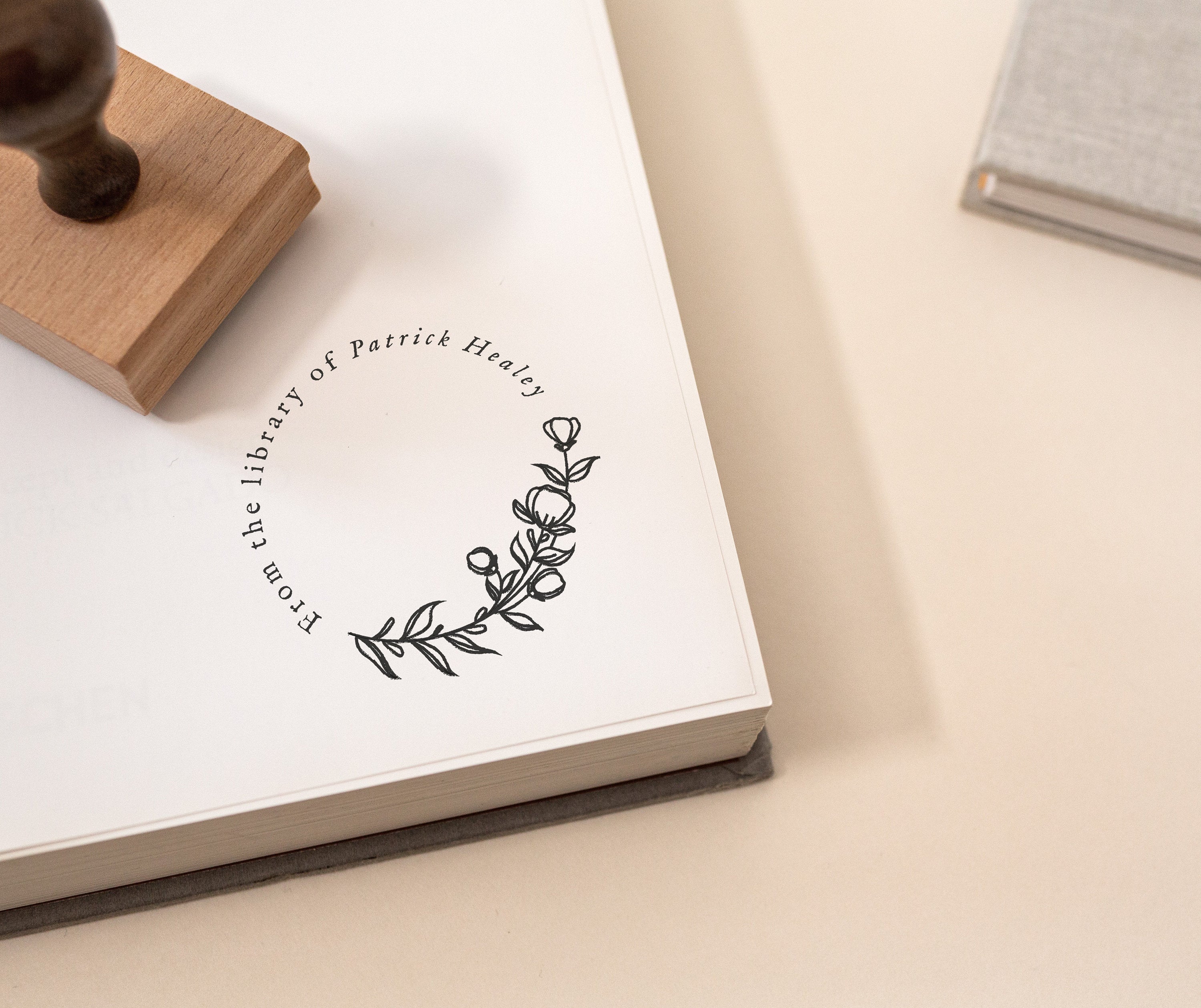 A custom library stamp with a design of a flower library motif, placed on an open book with a wooden handle on the side.