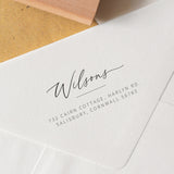 A close-up image of a custom handwritten address stamp on an envelope, showing the engraved return address in a stylish script.