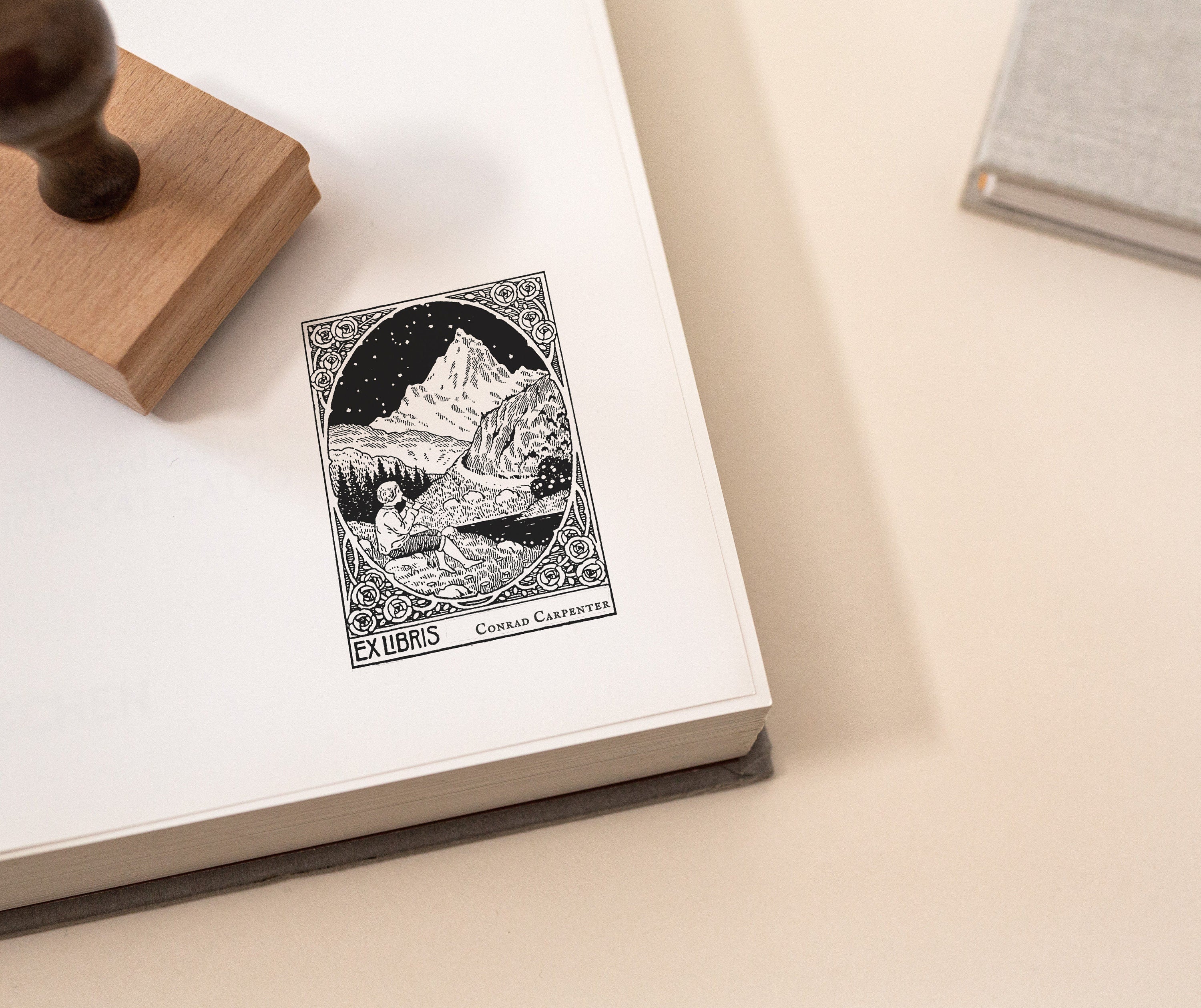 Beautiful custom rubber book stamp showing a young person playing a flute in a mountain scene, stamped on the right page of an open book