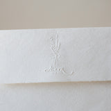 Floral couple initials wedding embosser impression on a handmade wedding envelope.