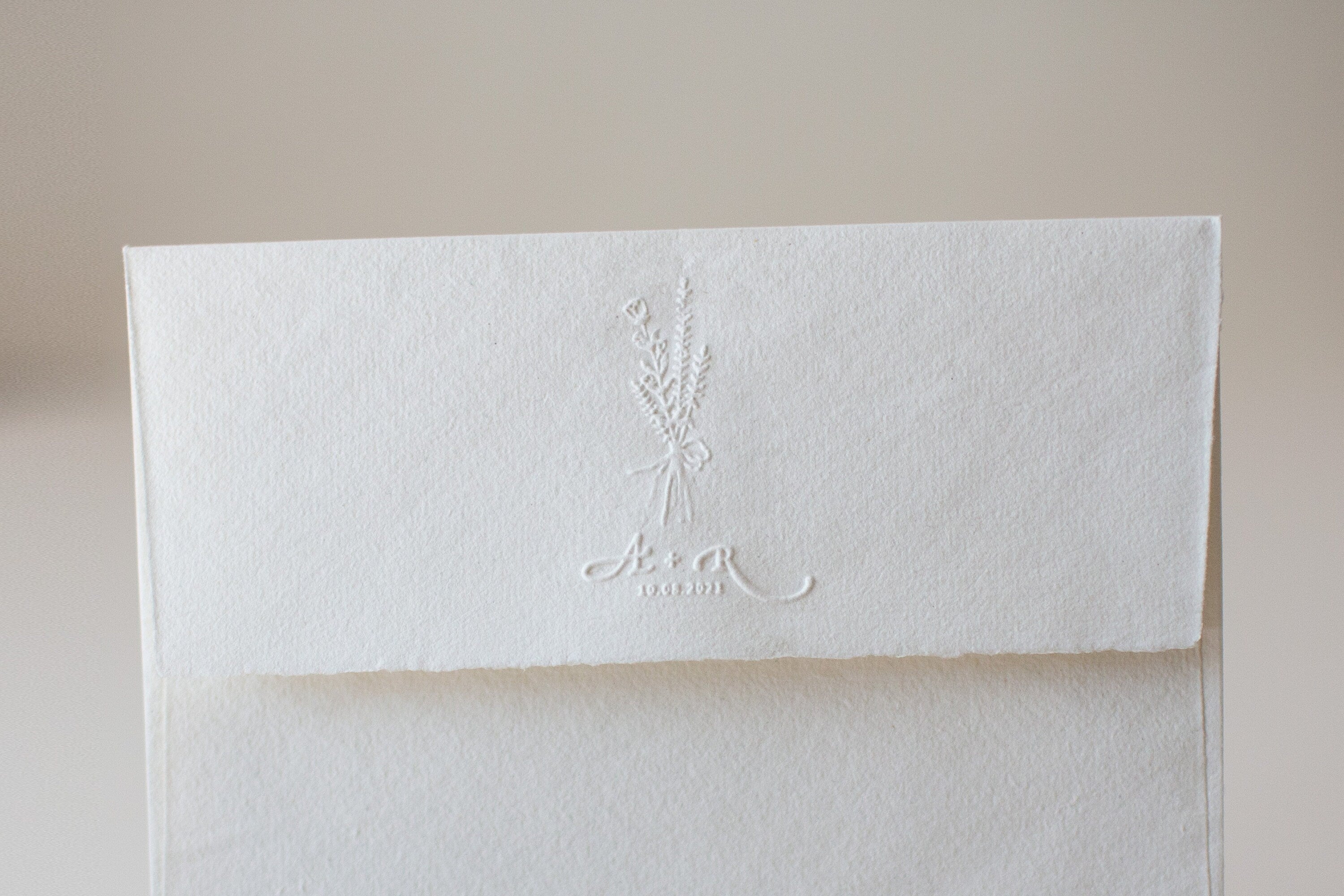 Floral couple initials wedding embosser impression on a handmade wedding envelope.
