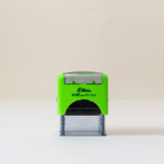 An eco-friendly green and black self-inking stamp with a custom logo, placed on a beige background.