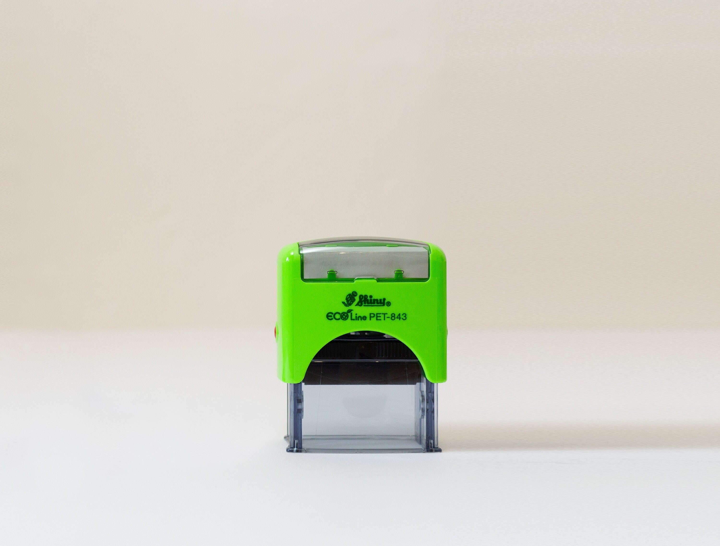 An eco-friendly green and black self-inking stamp with a custom logo, placed on a beige background.
