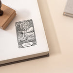 A custom library stamp with a tree and book design on a piece of paper, accompanied by a wooden stamp on top.