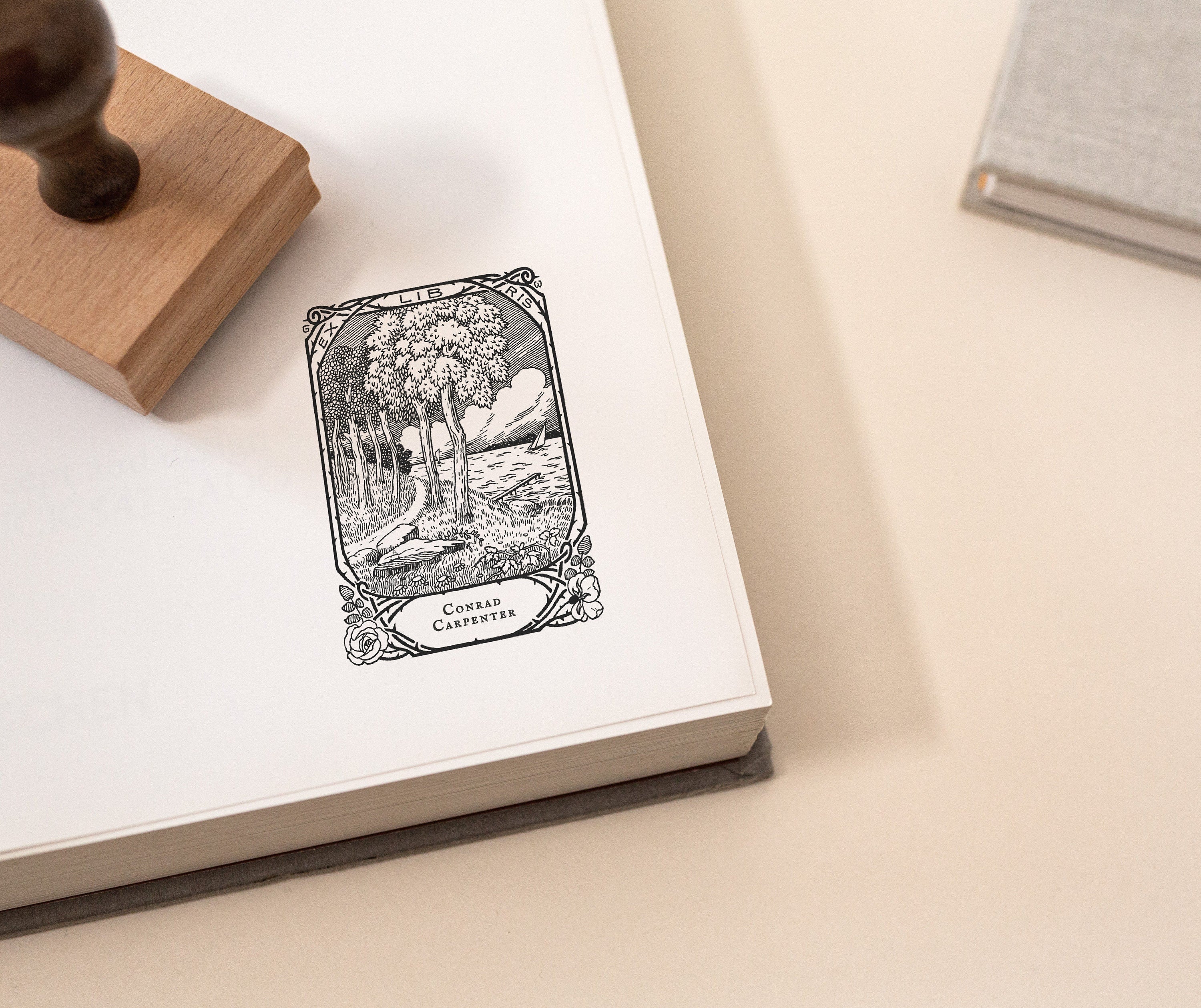 A custom library stamp with a tree and book design on a piece of paper, accompanied by a wooden stamp on top.