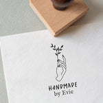 A custom rubber stamp with your custom text and a small floral design, stamped on a piece of paper with a wooden stamp in the background.