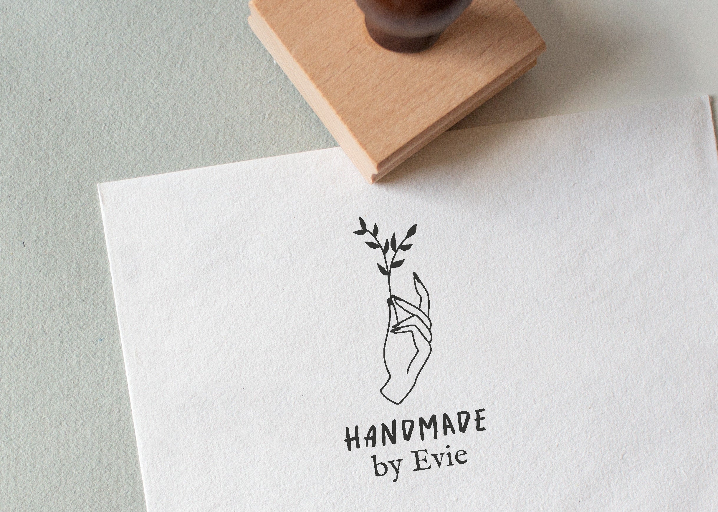 A custom rubber stamp with your custom text and a small floral design, stamped on a piece of paper with a wooden stamp in the background.
