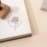 A custom book stamp with a hydrangea flower design, placed on an open book with a wooden handle on the side.