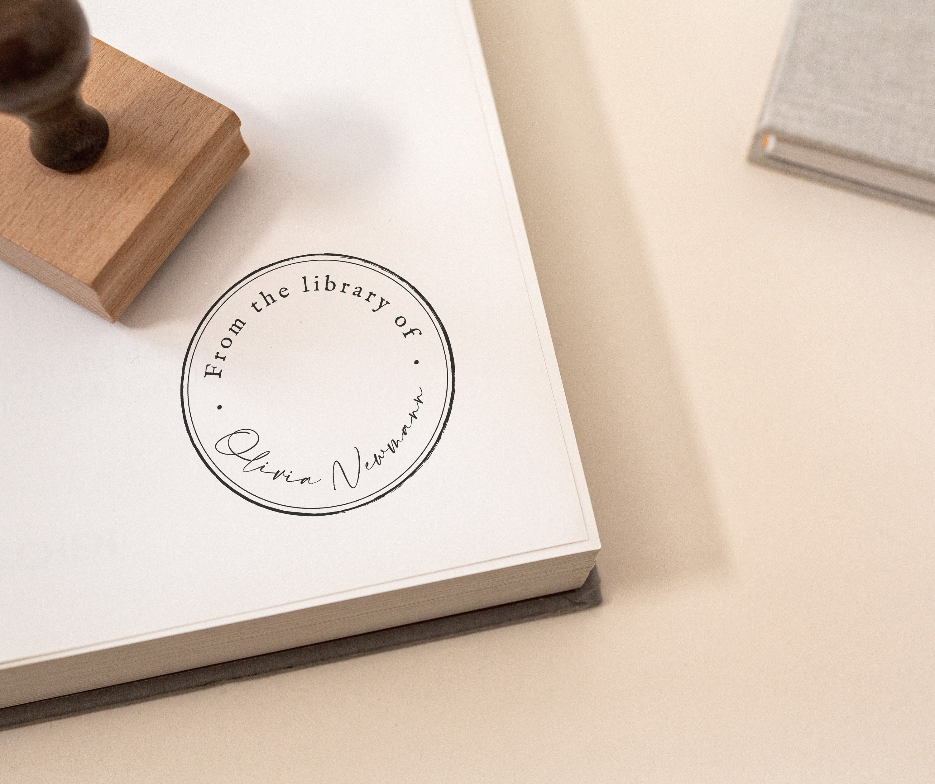 Minimal Script Book Stamp featuring a minimal design of a book stamp with a beautiful script and handwritten font stamped onto the pages of a book