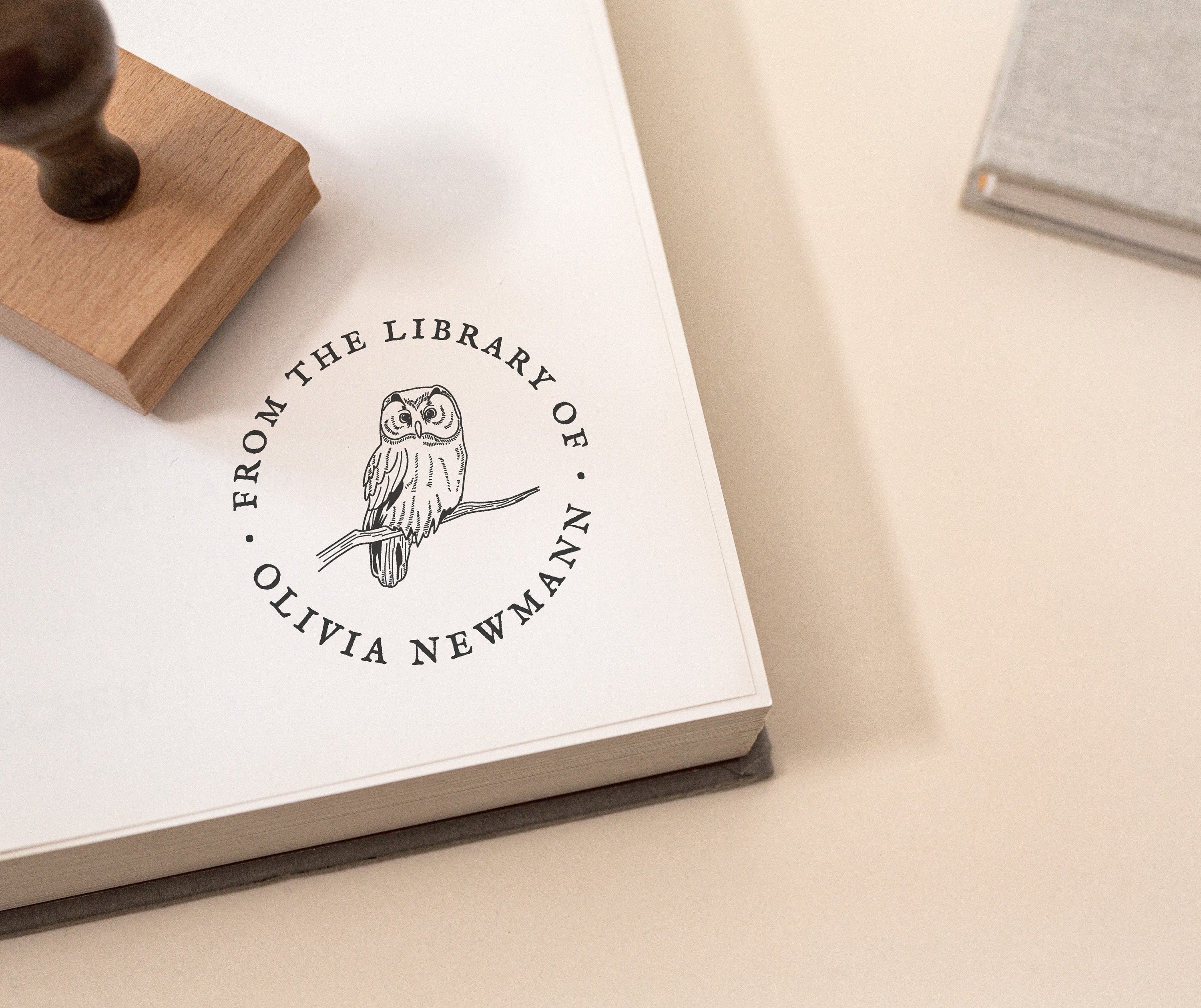 A custom library stamp with an owl design, placed on a book with a blurred background.