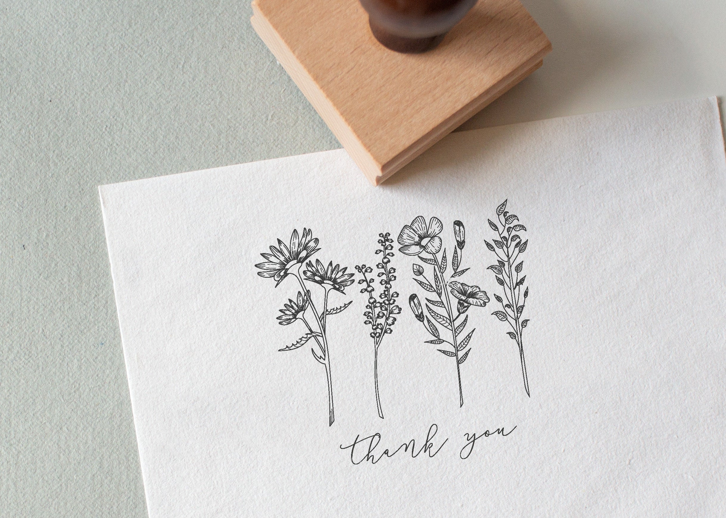 A custom floral-themed rubber stamp with the words 'Thank You' stamped on a piece of paper, accompanied by a wooden rubber stamp