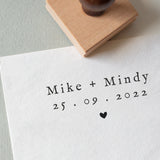 A personalized wedding stamp with bride and groom names and wedding date and featuring a little heart illustration stamped onto a white textured paper