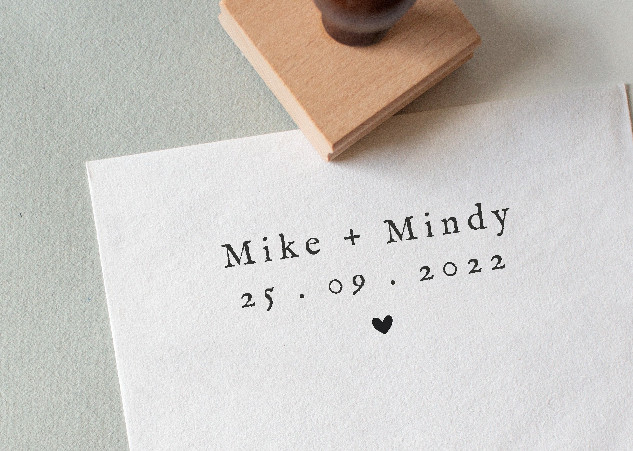 A personalized wedding stamp with bride and groom names and wedding date and featuring a little heart illustration stamped onto a white textured paper